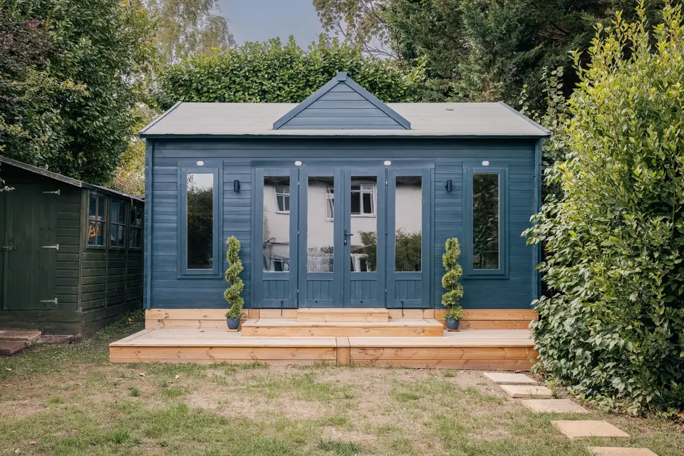 Navy apex garden room with full-height glazing, wall lights and a timber deck across the front