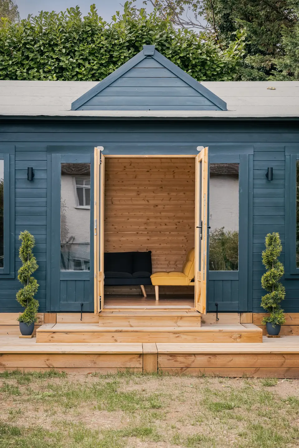 Double doors open on the navy garden room, showing a pine-lined interior with a sofa and armchair
