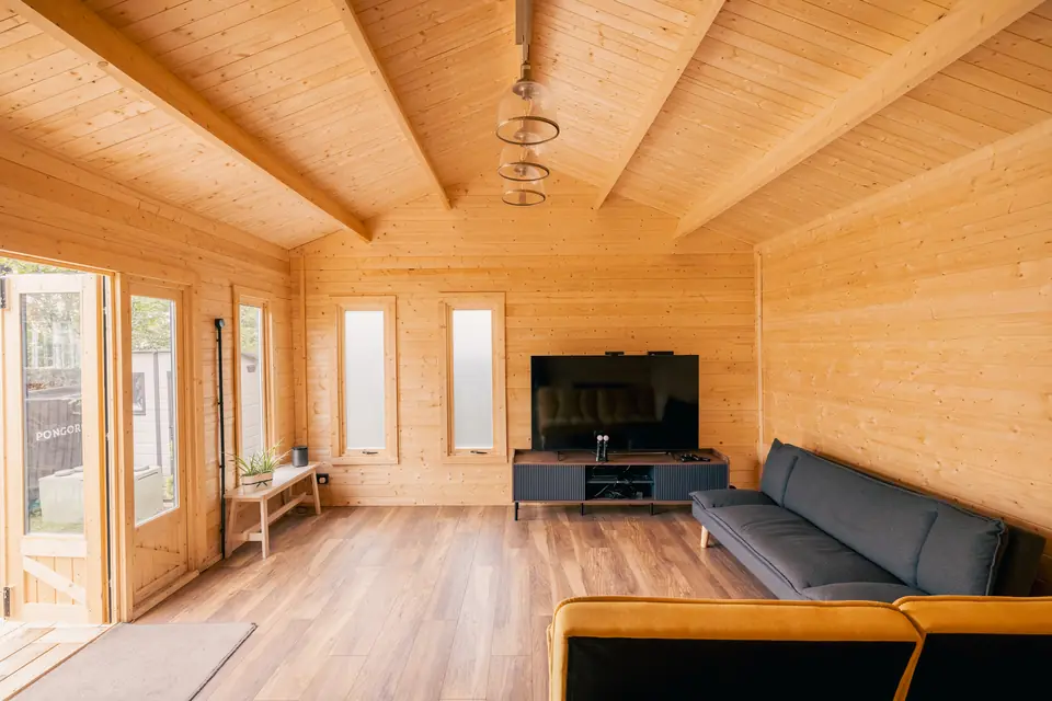 Pine-lined garden room with exposed roof beams, pendant lights, a television and sofas