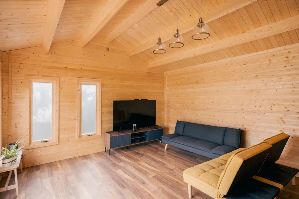 Pine-lined garden room furnished as a lounge, with pendant lights, a television, a sofa and a mustard armchair