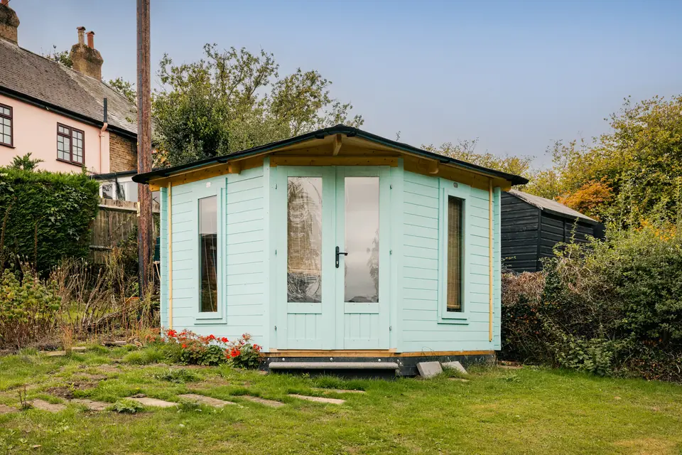 Pale mint corner garden office with a felt roof, glazed double doors and tall side windows