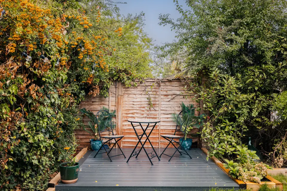 Small composite deck in a planted corner of the garden with a bistro table and two chairs