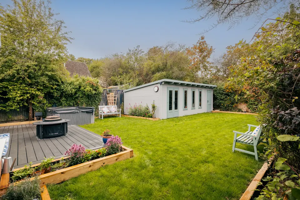 Renovated garden with a grey composite deck, new lawn, raised timber beds and a sage log cabin at the far end