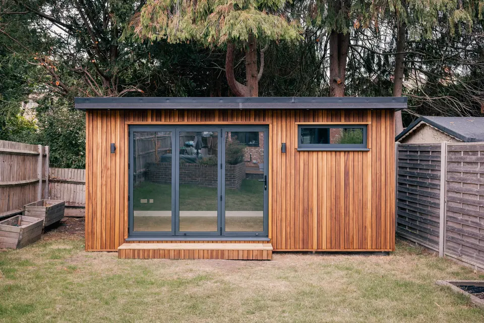 Garden studio with vertical timber cladding, closed anthracite bi-fold doors and a slim high window