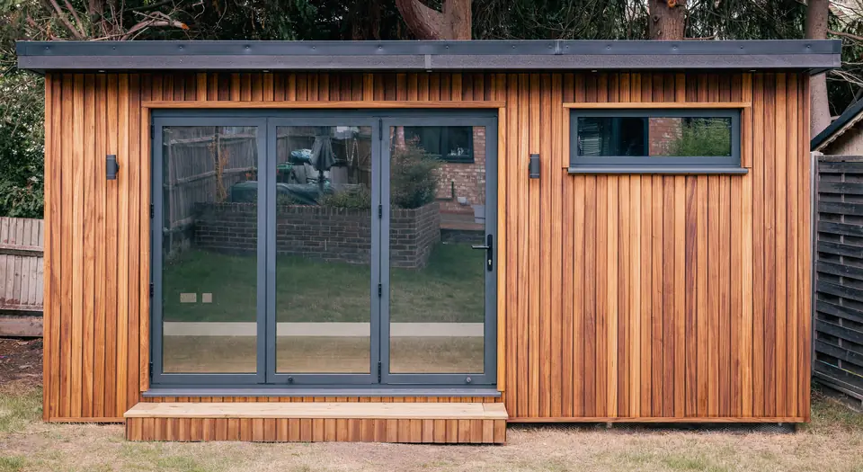 Timber-clad garden studio with anthracite bi-fold doors, a high window and a timber step