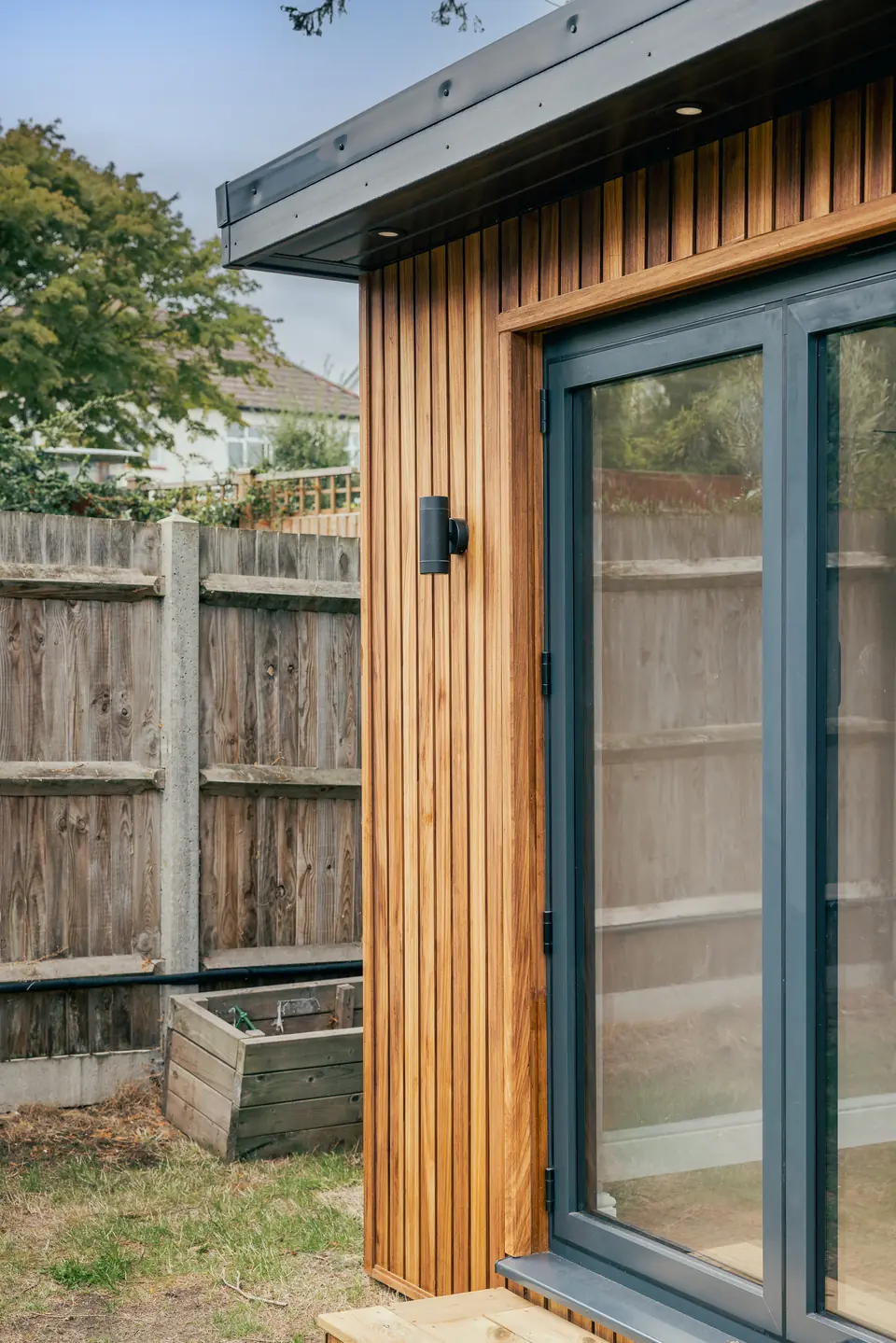Anthracite glazing framed by vertical timber cladding and a black wall light