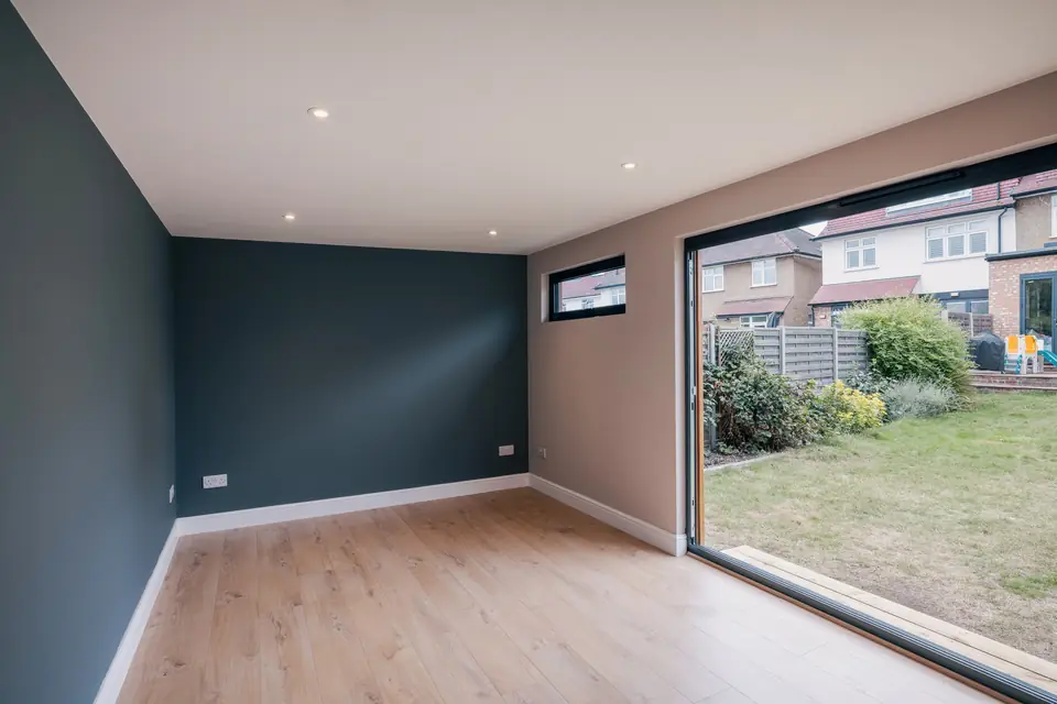 Inside the garden studio: dark feature walls, downlights and a wood-effect floor running to open bi-folds