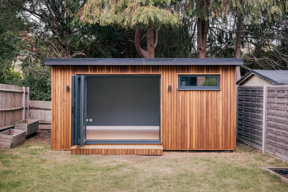 Timber-clad garden studio with anthracite bi-fold doors folded back to show a finished room inside